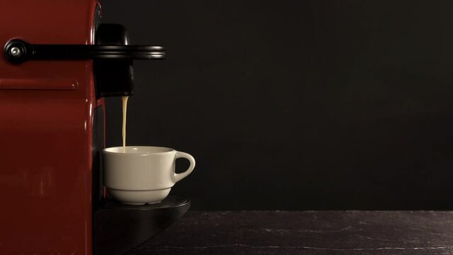 Red coffee machine making coffee on black background. When it finishes a hand enters and grabs the cup. 