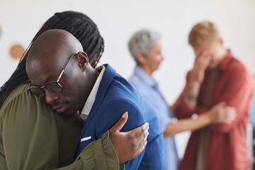 Side view at two African-American people embracing during support group meeting, helping each other...
