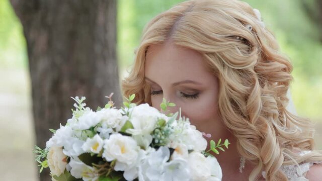 Bride with wedding bouquet in green summer forest.