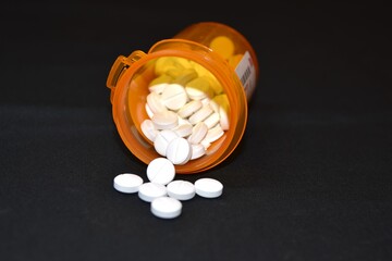 Medical concept prescription pills spilling out of bottle against a black background