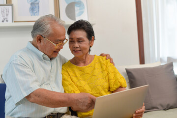 Fototapeta premium grandfather and grandmother used laptop to see photo or shopping on line in living room.Senior family concept.
