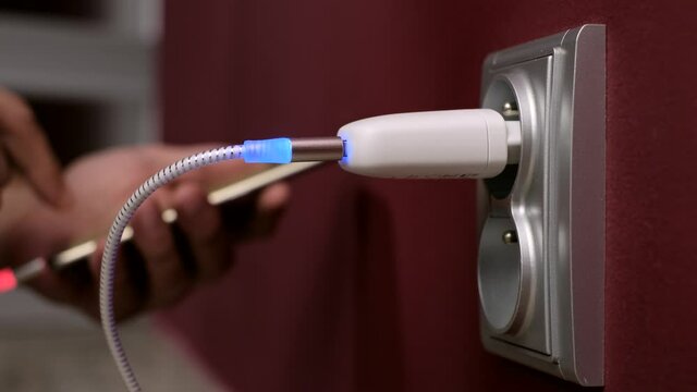 Typing and Charging Mobile Phone . Hand plug into electricity socket a power adapter cord usb device mobile phone cell charge
