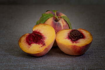 Two fresh yellow peaches on brown table, one whole and one cut in half, centered, with macro detail , side view- harvest still life, with plenty of copy-space