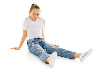 A little girl is sitting on the floor in a clean white T-shirt.