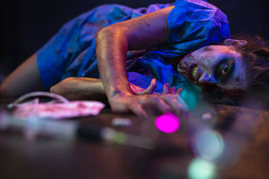 Halloween zombie with coronavirus Woman wearing face mask protective for Covid-19 reaching for the antidote on the floor. Horror infection concept