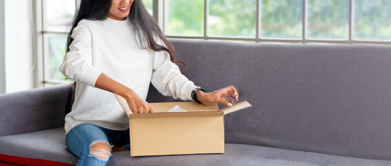 asian woman satisfied and smile unpack parcel on sofa at home.recieve goods delivery from online purchase store.online shopping omni channel post mail shipping concept - obrazy, fototapety, plakaty