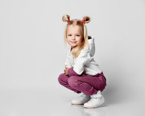 Smiling little blonde girl sitting and looking at the camera on a gray background.