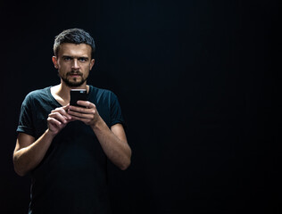 Portrait of a man on a black background with a phone in his hands