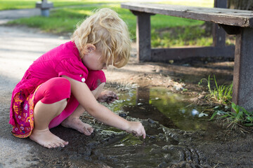 Child playing with dirty puddle barefoot in the park in summer. Happy childhood without electronic gadgets concept