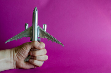 A hand holds a model of a silver airplane.