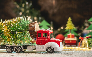 A red and white toy truck is transporting a Christmas tree against a background of lights and paper pines and snow