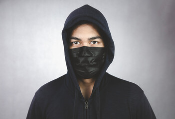 An image of a man in a hood or a jig on a dark gray background with a black mask covering his mouth and nose.