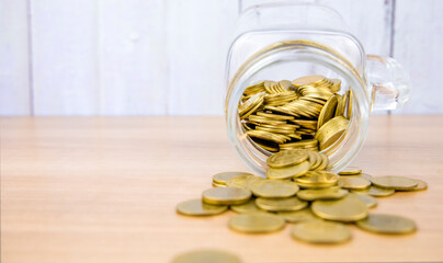 A pile of coins on a wooden table and a pile of coins in a glass jar.
