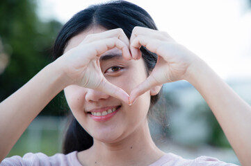 Happy Asian beautiful woman holding hands with heart shape and smiling woman with close-up love symbol.