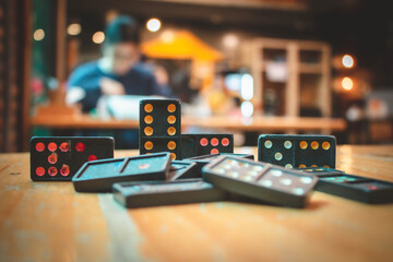 Close up old black color dominoes with colorful dot pieces. Falling Black Dominos on wooden desk with bokeh background.