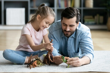 Happy father and little daughter playing with toy dinosaurs close up, sitting on warm floor with...