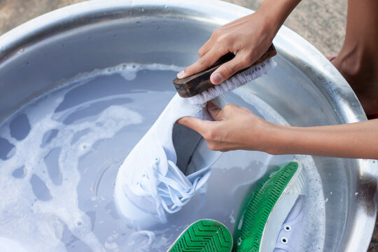 Hand of children washing the dirty shoes or sneakers in a bubble-filled basin.