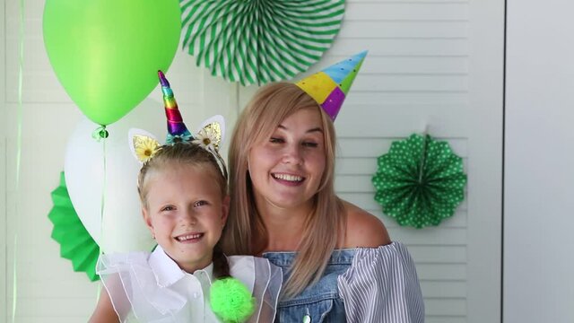 Mom and daughter are celebrating their birthday and waving at the camera and singing a song in the green design of the photo zone.