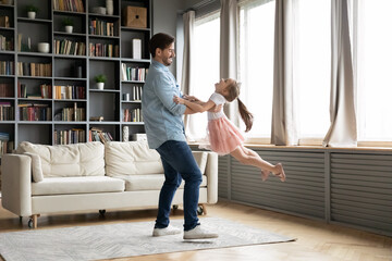 Loving father dancing with little daughter wearing princess dress and diadem, moving to favorite music, family spending leisure time together, dad spinning adorable child, holding in hands
