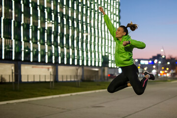 Fit girl exercise and jump on the street at night witl lights on background