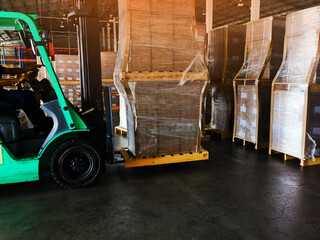 Worker driving forklift loading shipment carton boxes goods on wooden pallet at loading dock from...