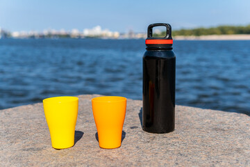 Two plastic caps (yellow and orange) and a thermos on a concrete barrier wall near a blue sea