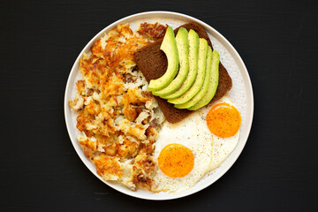 Tasty Homemade Fried Hashbrowns and Eggs on a plate on a black surface, top view. Flat lay, overhead, from above.