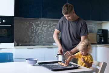 Young father and his small pretty daughter cooking together. Family is happily making cookies in the kitchen