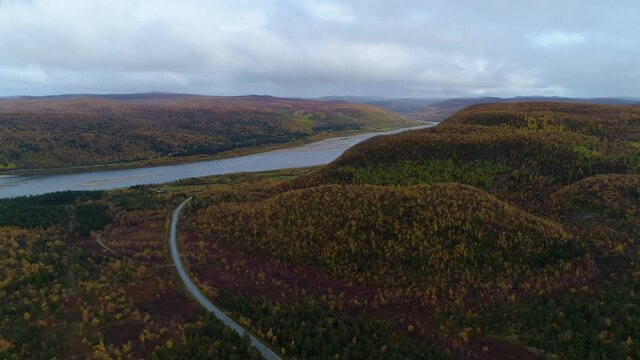Aerial, tracking, drone shot overlooking the Tenojoki river and the road 970 and the Finland-Norway border, on a,dark rainy, autumn day, near Utsjoki, in Lapland