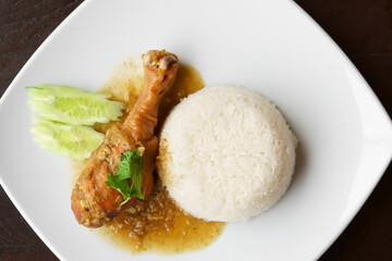Baked chicken drumstick rice juicy with cucumber and coriander or green vegetable on white dish and black wooden table for breakfast or lunch and dinner food in restaurant or food court on top view