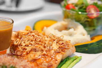 salmon fish steak grill in fried onions and white sesame with mashed potatoes and pumpkin combine to sauce and tomato vegetable salad on white dish for diet seafood and omega 3 in japanese restaurant