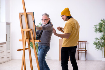 Old man taking lesson from young painter