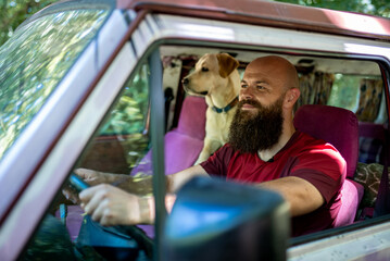 Young bearded man with dog, labrador retriever, traveling together on vintage minivan transport