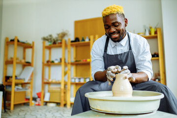 mixed race afro male potter with black apron sitting at workshop table potter