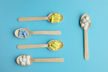 Colorful tablets and pills on wooden spoons. Pharmaceutical tablets in wooden spoons on a light blue background.