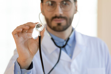 Close up serious young doctor holding stethoscope, medical checkup concept, therapist practitioner gp ready to examine lings or heart sounds with equipment, healthcare and health insurance