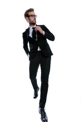 cool stylish man in black suit looking to side and fixing tie