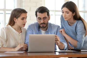 Businesswoman realtor consulting young couple at meeting, using laptop, pointing finger at screen, demonstrating presentation, man and woman discussing mortgage or loan conditions with manager
