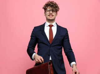 happy young businessman in suit holding suitcase and smiling