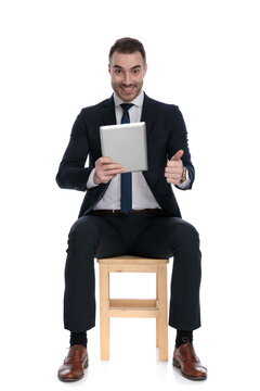 Happy businessman giving thumbs-up smiling and holding tablet
