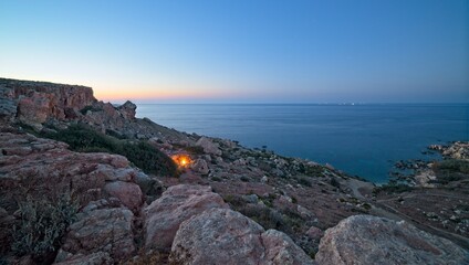 Fototapeta premium A campfire burns just after sunset at the rocky coastline of Selmun in Malta