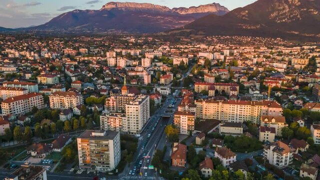 Annecy city aerial hyperlapse timelapse with moving traffic between buildings at street intersection, panoramic view at sunset with Alps mountains in background