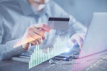 Double exposure of man hands holding a credit card and Forex graph drawing. Stock trading and digital fintech in Internet E-commerce concept.