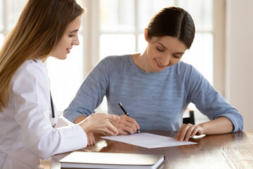 Obraz premium Smiling young woman signing medical insurance agreement at meeting, making deal with doctor, satisfied positive patient putting signature on documents, sitting at table, healthcare concept