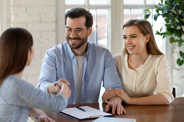 Happy young married couple making successful deal with realtor or financial advisor, planning...