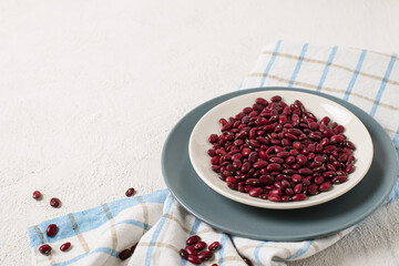 Red beans in a plate on a checkered towel on a white textured background. Space for text.