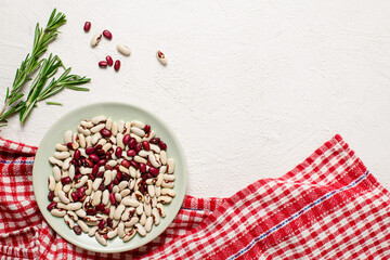 White and red beans in a plate on a checkered towel on a white textured background. Top view. Space for text.