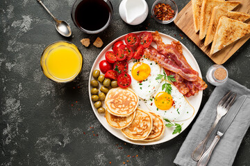 American breakfast with two fried eggs,pancakes,tomato salad,bacon, toast,orange juice and coffee.
