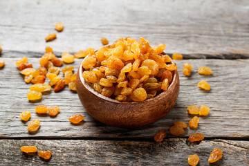 Golden dried raisins in wooden bowl on a wooden table.