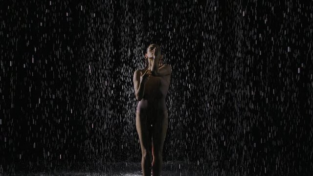 Female dancer perform contemporary dance under the drops of water rain. Wet female dancer moves gracefully in the studio under the rain water. Slow motion. Close up.